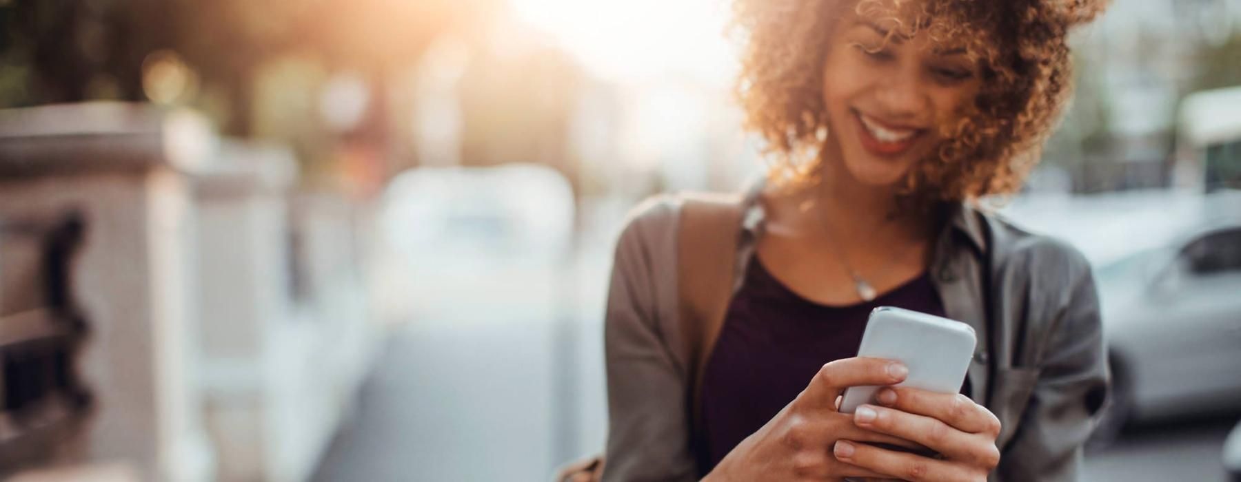 woman texts on her phone as she walks through the city